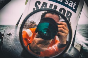 May 22, 2015. Leg 7 to Lisbon onboard Team Alvimedica. Day 05. OBR Amory Ross' reflection on the stern camera lens. The drag race northeast towards the eastern edge of the ice exclusion zone continues with the front five all still within a few miles of each other.